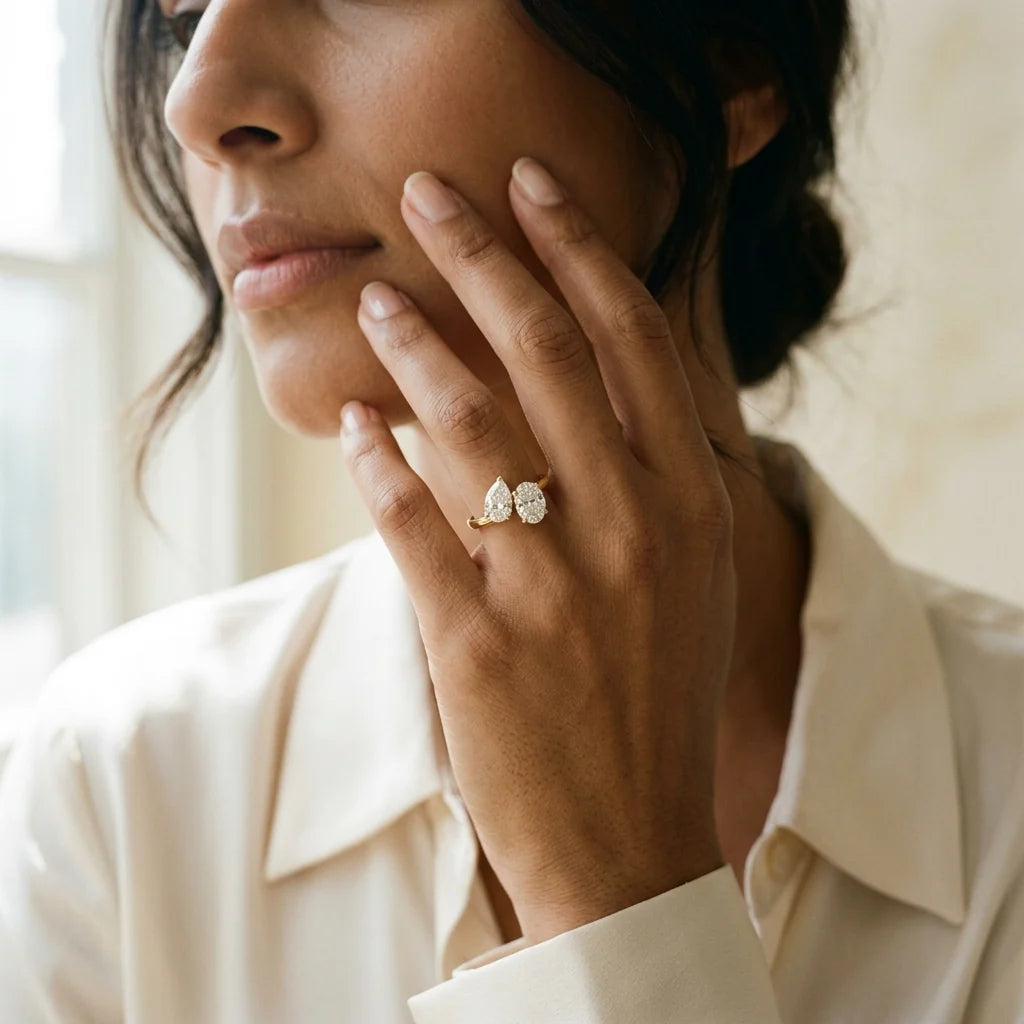 Toi et moi ring with a pear-cut and an oval-cut diamond facing each other on an 18k yellow gold band, white studio background