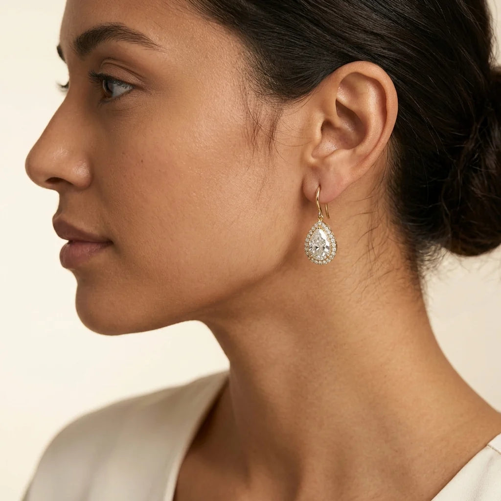 Pair of pear-shaped diamond drop earrings with pavé halos in 18k yellow gold on a white studio background