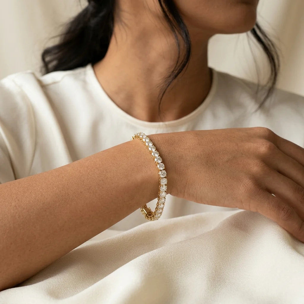 Round brilliant diamond tennis bracelet in 18k yellow gold with a box clasp on a white studio background