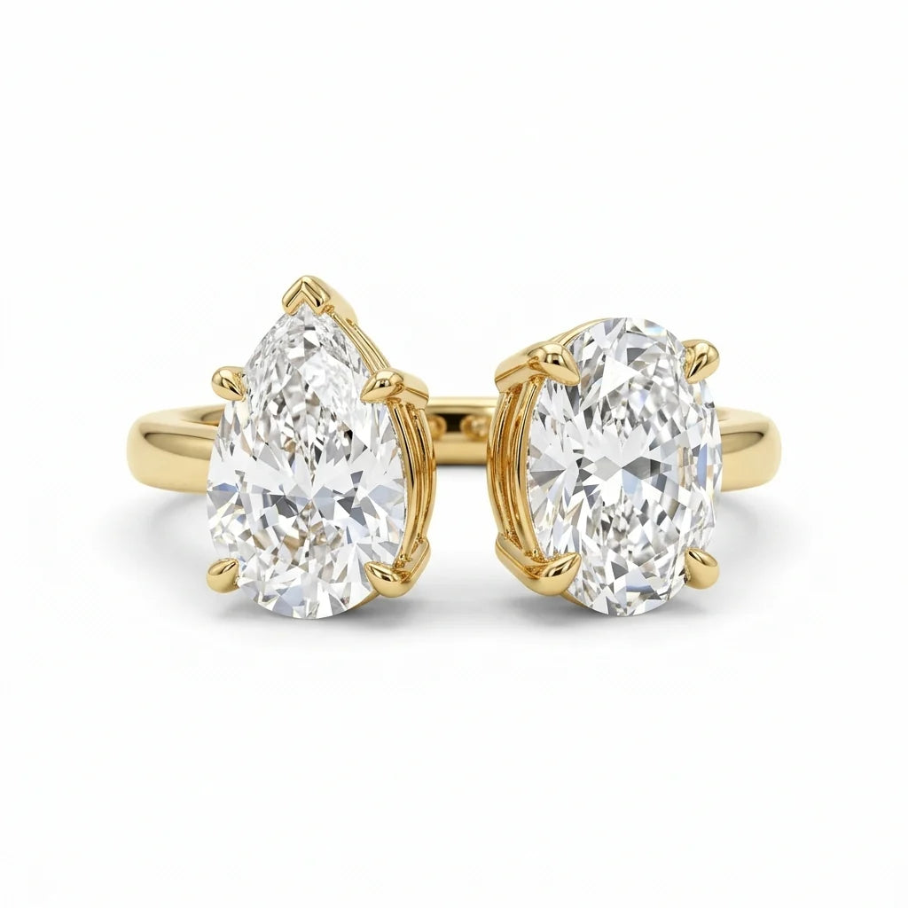 Toi et moi ring with a pear-cut and an oval-cut diamond facing each other on an 18k yellow gold band, white studio background